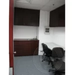 A small office space with white walls, three chairs around a desk, overhead cabinets, and a closed door on the left side.