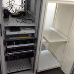 A close up of a computer server rack with wires, hard drive and a shelf