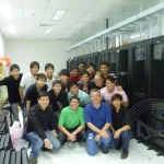 A group of IT technicians from A-ChieveMent Solution posing for a photo in a server room full of racks and housings